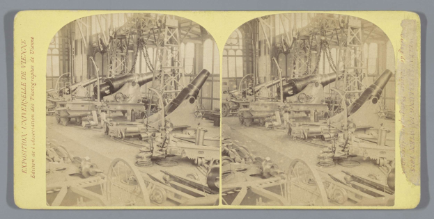 Schwarzes und weißes Foto eines alten Fabrikinneren mit einem gro├čen Geschütz in der Mitte, umgeben von zus├Ątzlichen Geschützen, Metallstangen und verstreuten Gegenst├Ąnden auf dem Boden, mit Text auf der linken Seite.