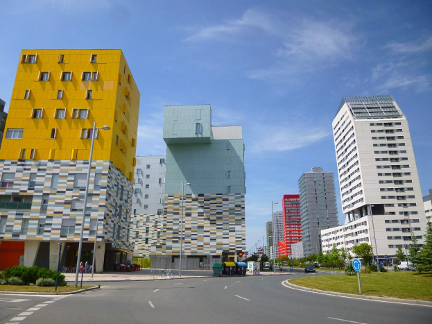 Eine Stadtstraße mit hohen Gebäuden, die als Teil der Universität Rotterdam bezeichnet sind, Straßenlaternen, Verkehrspolizeischilder, Autos, Informationsschilder, Büsche, Bäume und eine bewölkte Himmel.