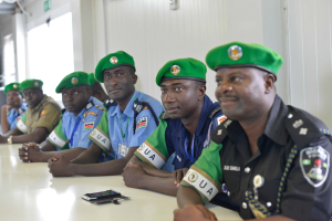 Gruppe von Polizeibeamten, die während einer Schulung an einem Tisch sitzen, mit Mobiltelefonen und anderen Gegenständen auf dem Tisch, in einem Raum mit Fenstern und Deckenleuchten.