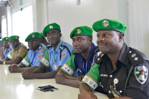Gruppe von Polizeibeamten, die während einer Schulung an einem Tisch sitzen, mit Mobiltelefonen und anderen Gegenständen auf dem Tisch, in einem Raum mit Fenstern und Deckenleuchten.