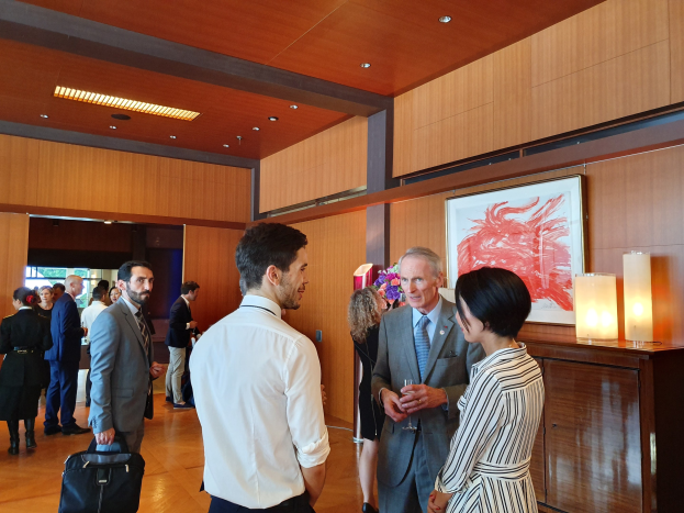 Eine Gruppe von Menschen, die in einem Raum mit einer hölzernen Wand mit einem Fotorahmen und Beleuchtung sprechen, einige halten Taschen auf einer Kunstausstellung im Nationalmuseum Singapur.