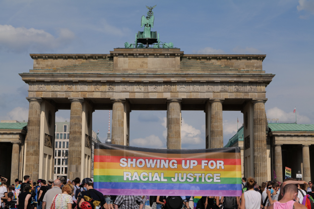 Eine Gruppe von Menschen steht vor dem Brandenburger Tor in Berlin, Deutschland, mit einer Schilder mit der Aufschrift "Racial Justice".