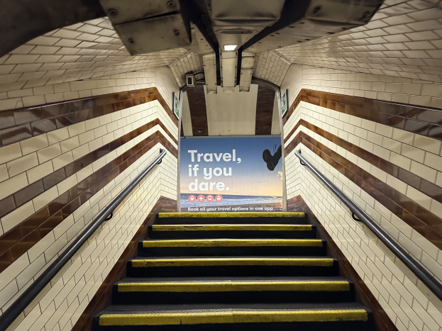 Eine Treppe in einer U-Bahn-Station mit einem 'Reise, wenn du dich traust'-Schild oben, flankiert von Geländern und Stationwänden im Hintergrund.