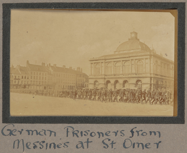 Deutsche Kriegsgefangene aus Messines vor einem Gebäude mit einem klaren blauen Himmel im Hintergrund, mit Text am unteren Rand.