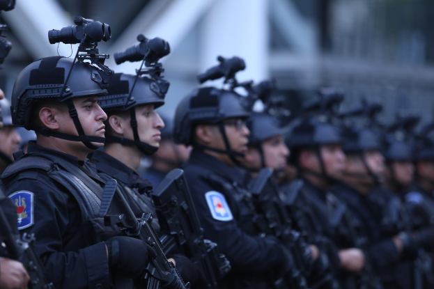 Eine Gruppe von Polizisten in schwarzen Uniformen und Helmen mit Waffen in einer militärischen Umgebung.