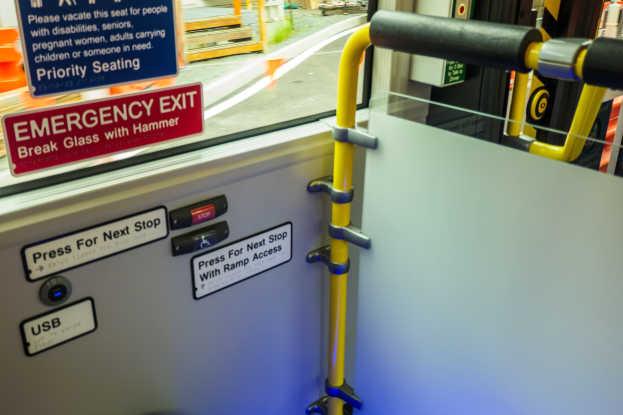 Notausgangsschild an der Seite eines Zuges mit einer Tür, Griff und Glasfenster, das die Außenlandschaft zeigt.