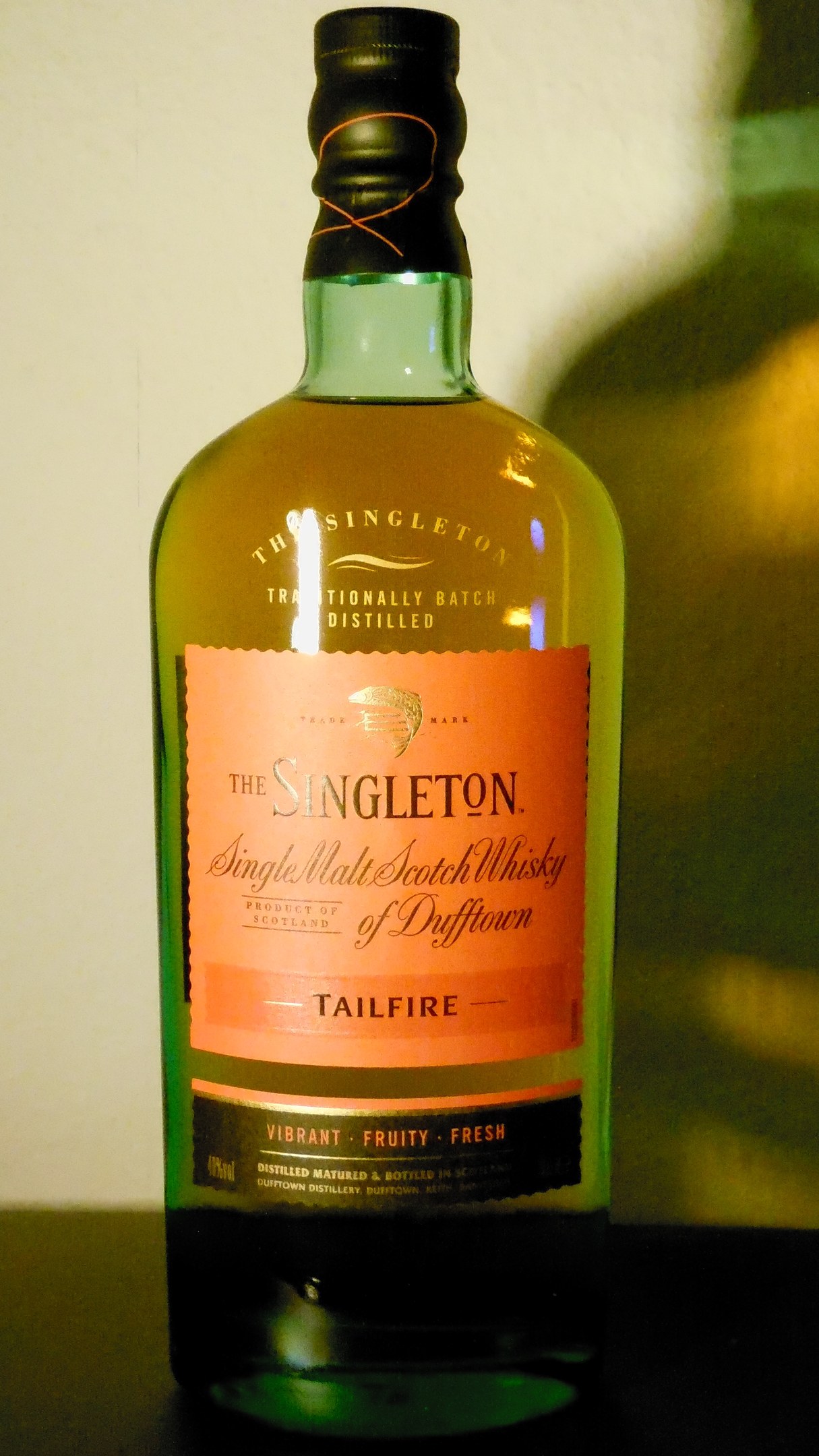Eine tiefe bernsteinfarbene Flasche Singleton of Dufftown Tailfire Single Malt Scotch Whisky mit einem schwarzen Etikett, das ein Löwen- und Schlosswappen zeigt.