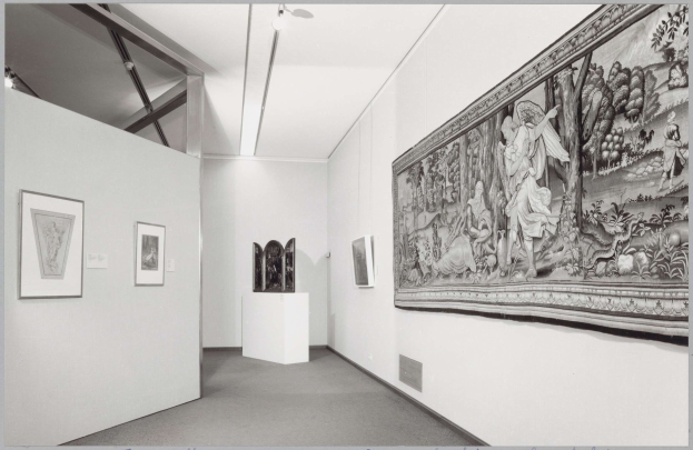 Schwarzes und weißes Foto eines Museumsraums mit einem großen Wandteppich, gerahmten Kunstwerken an den Wänden, Sockelausstellungen, Deckenbeleuchtung und dem Text "Museum of Fine Arts, New York City" unten.