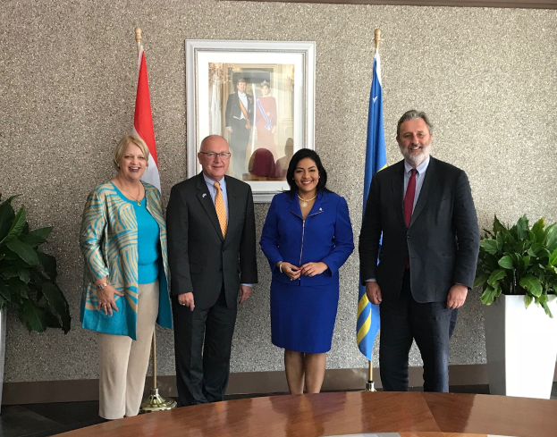 Eine Gruppe strahlender Menschen um einen Tisch mit Papieren herumstehend, umgeben von Fahnen, Topfpflanzen und einem Fotorahmen an der Wand, feiert die Unterzeichnung eines Memorandums von Verständnis zwischen den Vereinigten Staaten und Kanada.