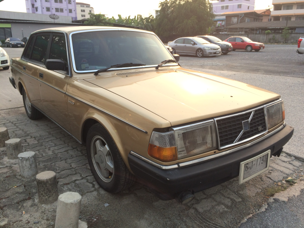 Ein goldfarbener Wagen parkt an der Seite einer Straße mit Gebäuden, Bäumen und einem klaren blauen Himmel.