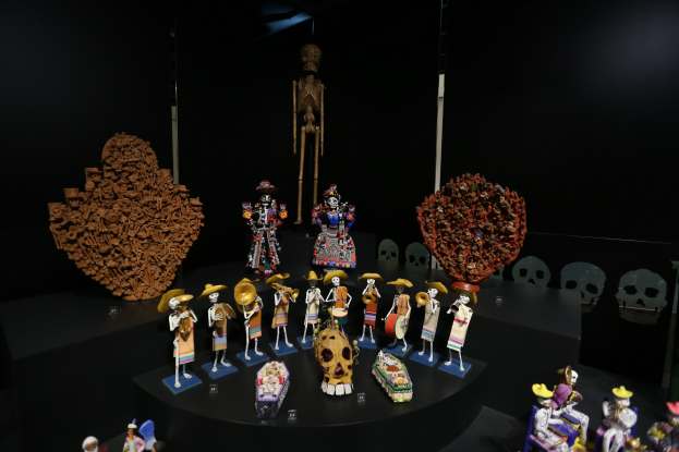 Vitrine voller verschiedener Spielzeuge, darunter Puppen und Schädel, vor einem dunklen Hintergrund.