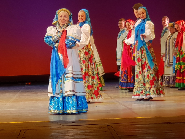 Gruppe von Menschen in leuchtenden, detaillierten traditionellen ukrainischen Kostümen auf einer Bühne, die fröhlich und glücklich aussehen.