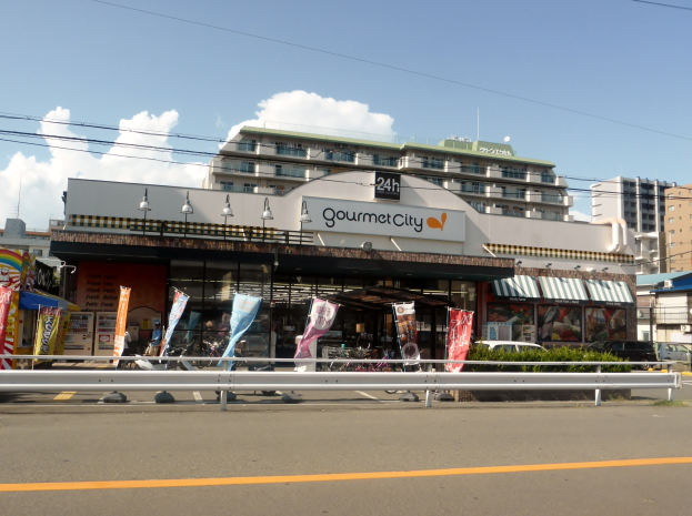 Eine belebte Stadtstraße mit Gebäuden, Straßeneinrichtungen, Fahrzeugen, Grünflächen und einem Restaurant, das Essen in seinem Schaufenster präsentiert.