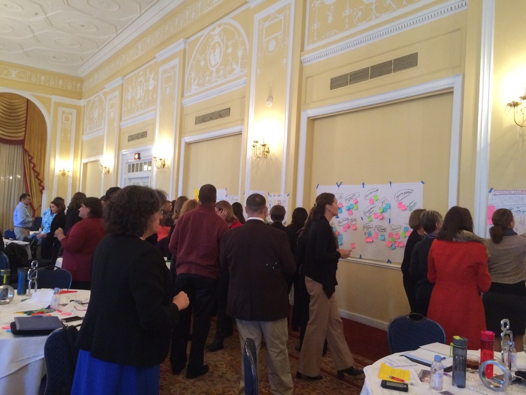 Eine Gruppe von Menschen betrachtet Plakate und Schaubilder an einer Wand in einem, was wie ein Kunstmuseum aussieht.