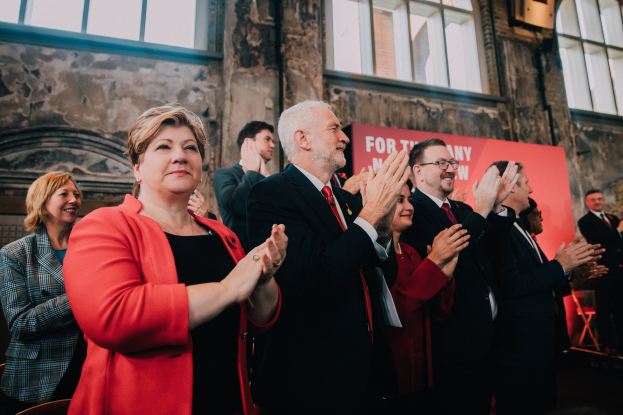 Eine Gruppe von Menschen, die vor einem Publikum jubelnd klatschen, mit einem Banner im Hintergrund, das einen Wahlsieg anzeigt.