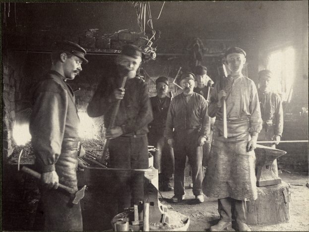 Eine Gruppe von Männern in einer Schmiede, jeder hält einen Hammer in der Hand.