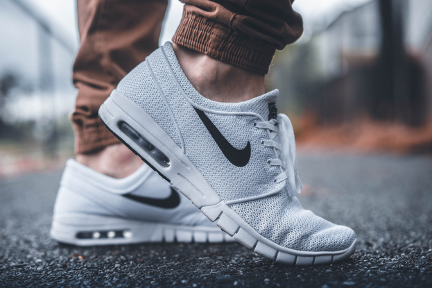Eine Person trägt Nike SB Stefan Janoski Max Schuhe in Wolf Grau/Schwarz-Weiß vor einem unscharfen, träumerischen Hintergrund.