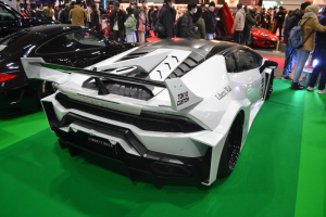 Ein Lamborghini Aventador LP700-4 Superveloce auf der Geneva Motor Show, umgeben von Menschen in verschiedenenfarbiger Kleidung, mit beleuchteten Schildern im Hintergrund.